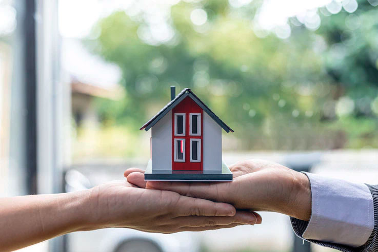 Seguro Residencial - Mãos feminina e masculina sobre postas embaixo de maquete de casa